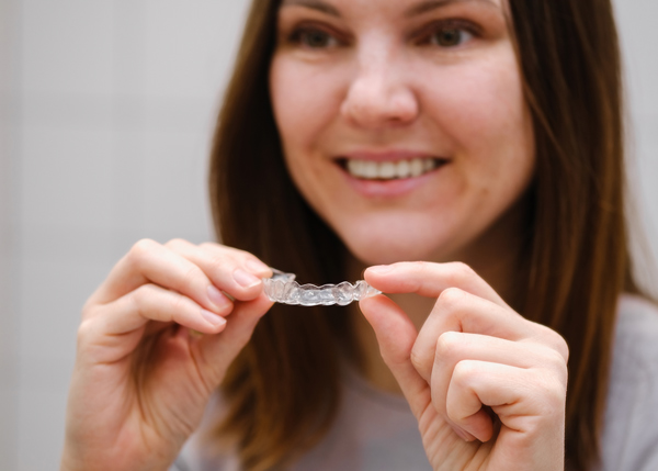 woman holding a clear aligner smiling showcasing teeth transformation effects 2 dental options