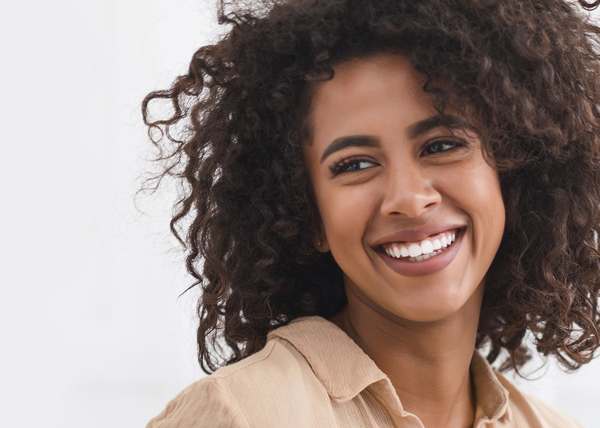 smiling woman with curly hair in a natural setting showcasing happiness and beauty three ways to enhance smile