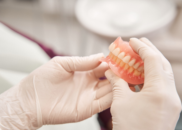 dentist holding removable dentures with eight teeth visible showcasing dental hygiene and prosthetics