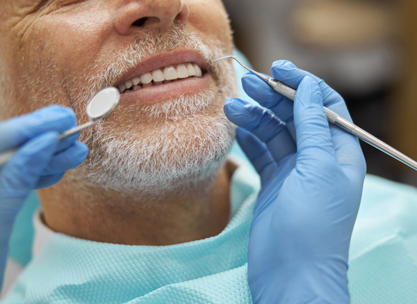 dentist examining smiling senior patient during dental checkup with tools for oral hygiene and two hands holding instruments