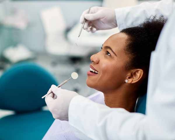 happy patient smiling during dental checkup with dentist holding tools and equipment for oral care and hygiene in a modern clinic setting