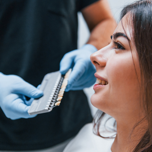 woman at dental appointment comparing tooth shades with dental professional holding shade guide for cosmetic dentistry